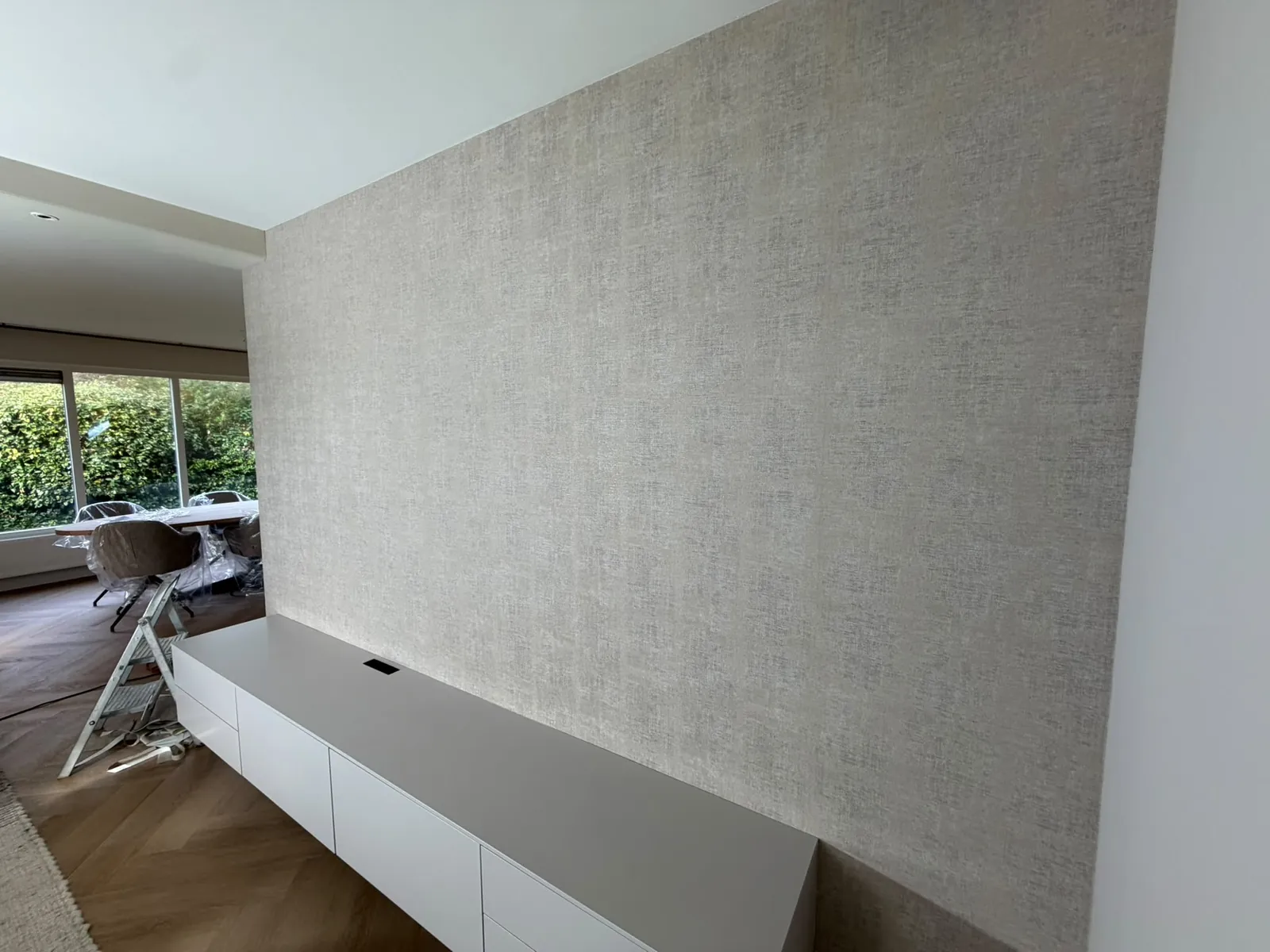 Lichte woonkamer met een vers behangen wand achter een wit dressoir
