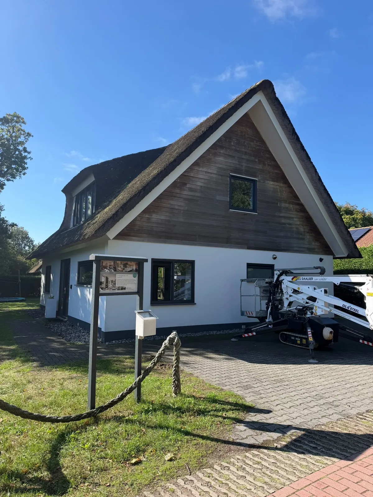 Wit huis met rieten kap, een hoogwerker staat ernaast op de oprit