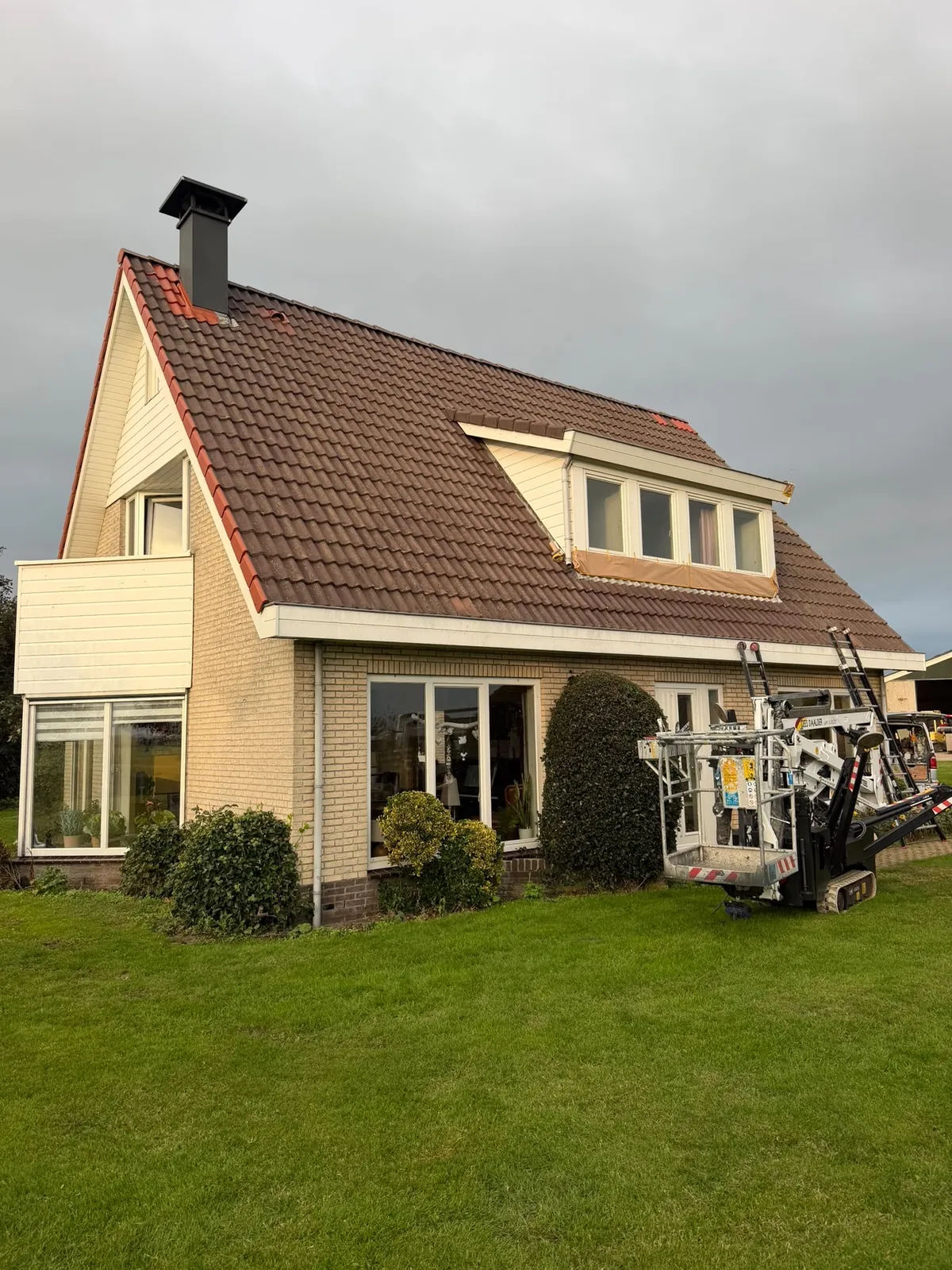 Woning met witte dakkapel en kozijnen, een hoogwerker staat in de tuin