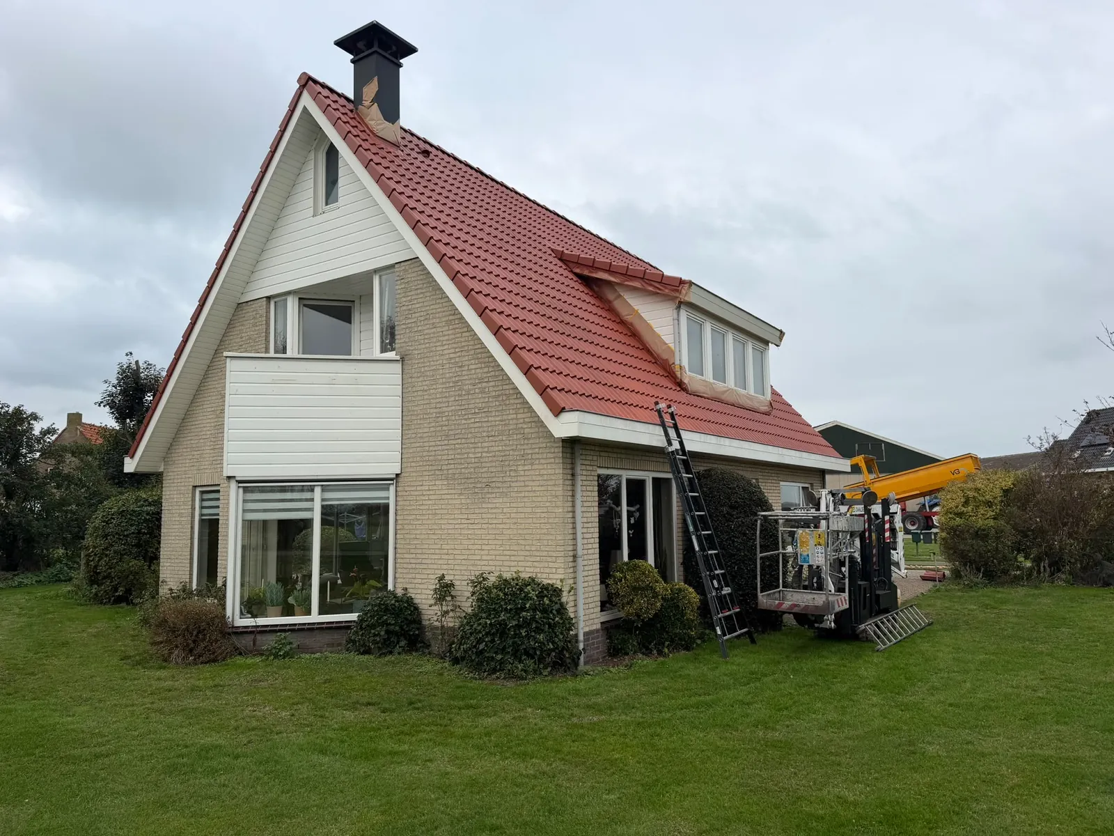 Woning met rood pannendak en witte gevelbetimmering, met ladder en hoogwerker